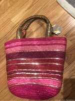 Front view of large pink and gold straw tote handbag with horizontal stripes and braided handles.