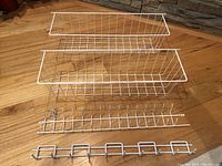 Photo of two white wire baskets and two white tie/scarf racks laid out on wood floor.