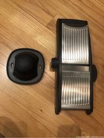 Top view of the mandoline slicer and hand guard on the floor showing the stainless steel ribbed slicing platform and black plastic components.