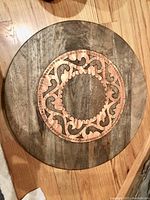 Top view of round solid wood Lazy Susan featuring decorative brass inlay at center on wood floor