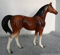 Side view of ceramic horse statue showing brown body, black mane and tail, white lower legs, and paint chips.