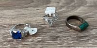 Three rings displayed side by side: blue stone ring, Charmed Aroma silver rings, and vintage green stone ring showing wear and tarnish