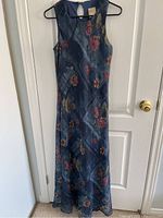 Full view of the sleeveless, floor-length blue crepe dress with floral pattern hanging on hanger