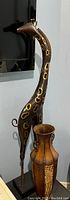 Tall metal giraffe sculpture painted black with gold circular accents and mounted on rectangular base, standing next to vase