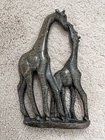 Top view of dark soapstone giraffe sculpture showing two giraffes intimately posed with necks bent toward each other, minor chips visible on one ear and side, placed on carpet