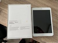 White Apple iPad Mini next to its original box showing 16GB capacity label on box's back.