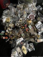 Overview of the lot showing several dozen enamel and metal lapel pins individually bagged or loose on a dark surface