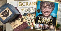 All four items visible including Scrabble box, mini cauldron mug box, notebook, and magazine together on a light surface