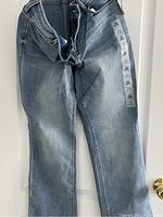 Front view of light blue denim Old Navy jeans showing jean front with zipper, button, pockets, and tags attached along the side seam.