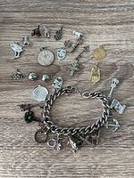 Charm bracelet laid on wood surface showing all individual charms, including gold-tone hamsa hand, horse, anchor, and theater mask.