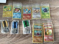Assorted Pokémon cards and three sealed Star Wars promotional medals with colored fabric straps arranged on wooden surface