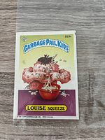 Garbage Pail Kids sticker card titled 'LOUISE SQUEEZE' with character squeezing pimples and foamy substance in bowl. Marked 1987 Topps.