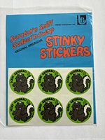 Image showing the sealed pack of six round green stickers with cartoon skunk images and 'Scent-Sational!' text on blue backing card.