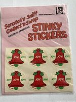 Front of sealed pink package with six red bell 'Joy!' stickers, Trend Enterprises branding, and scratch and sniff label.