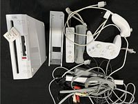 Photo of Nintendo Wii console, stand, controllers, sensor bar and cables laid flat on black surface.