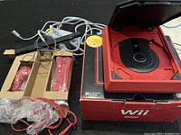 Top view of red Nintendo Wii Mini console opened showing disc tray, controllers in original packaging, and cables next to the original Wii Mini box.
