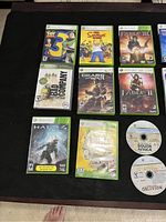 Photo showing 9 Xbox 360 game cases and 2 loose discs on a black surface, items have visible scratches.