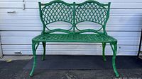 Front view of full green wrought iron bench against white backdrop