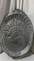Front view of a large silver metal platter shaped and textured like a turkey with a red eye detail.