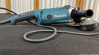 Full view of the angle grinder showing the blue and black body and silver head with side handle attached.