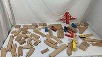 Photo showing complete set of wooden train track pieces, trains, red wooden train bridge, and wooden train accessories arranged on white surface.