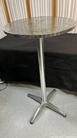 Full view of the metal bar/tall table showing round engine turned top and metal pedestal base.