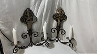 Pair of fleur-de-lis shaped metal wall sconces with mirrored backplates and two white taper candles each