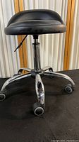 Front angled view of the black rolling adjustable shop stool showing padded seat and chrome base with caster wheels.