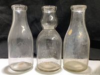 Full view of the three vintage one quart milk bottles from California dairies on black background.
