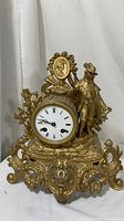 Front view of the ornate gold gilt Victorian mantel clock with figure and floral design.