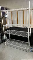 Front view of white wire shelving rack with four shelves set up against a wall.
