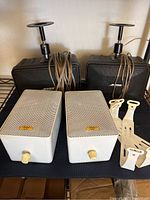 Pair of Acoustic Audio model 1251 cream/white speakers with perforated metal grills and control knobs in front, plus mounting brackets and Bose black speakers behind with cables wrapped around.