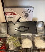 Overview photo showing the Hoop II car side step kit box, Chevrolet grille plate with side marker lights, and bags of hardware and fog light bezels.