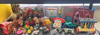 Wide view of assorted children's toys including dolls, toy vehicles, figurines, Fisher Price Chatty Telephone, and the red and blue Fisher Price playhouse in the back