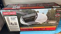 Photo of the unopened Craftsman garage door opener box showing product image, branding, motor power (1/2 HP), and chain drive type.