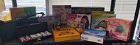 Wide shot of toys and games collection on table showing boxes of Lego Friends, IQ Builders, Operation Escape Room, Trolls game, and others.