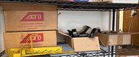 Shelf view showing yellow metal rail hardware and black curved replacement parts next to Acro Building Systems boxes