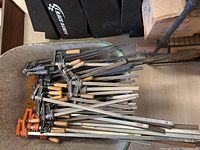 Overview of pile of assorted bar-style pipe clamps in wheelbarrow (wheelbarrow not included).