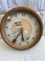 Front view of round wooden framed clock with Swedish Chef illustration and utensil shaped hands.