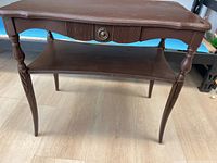 Front and side view of wooden Victorian style side table showing carved legs, ribbed drawer front with metal pull handle, and lower shelf.