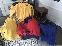 Three adult ski jackets and one yellow rain coat displayed on a chair.