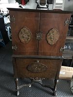 Front view showing the entire antique wooden cabinet with floral painted panels on doors and brass hardware.