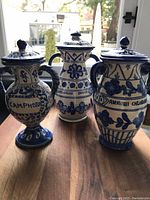 Photo showing three large apothecary jars with lids, hand-painted blue floral and leaf motifs on white base, each labeled with content names.