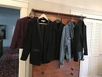 Photo of five women's jackets hanging on wooden hangers over dresser: burgundy tweed bolero, black leather trim blazer, vintage suit jacket, large denim jean jacket, and black pinstripe jacket