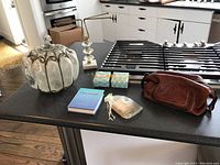 Wide shot showing all items on kitchen island: glass pumpkin, towel stand, leather bag, soaps, book.