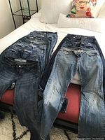 11 pairs of women's jeans in various shades of blue denim laid out on bed and chair