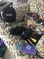 Various ski gloves and 4 pairs of ski goggles arranged on patterned couch upholstery