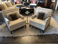 Pair of mid century vintage chairs on a white shag rug. Upholstered in striped seafoam green/gold fabric with wooden legs. No throw pillows included.