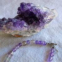 Close-up view of amethyst geode with purple crystalline interior and bracelet with beads and sterling silver findings.