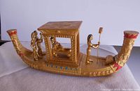 Side view of the gilt wooden boat sculpture with figures on board, showing the covered cabin with reclining Cleopatra and two standing figures at the back and the decorative prow.